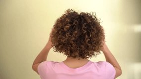 Rear view of female model, with curly afro hair, looking at the camera while playing with her hands on her head. Caucasian woman wearing pink t-shirt. - Powered by Shutterstock - Get 15% off with code: PIKWIZARD15