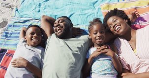 Video of happy african american family lying on beach and laughing. Holidays, vacations, relax and spending quality family time together concept.