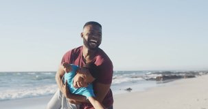 Video of happy african american father and son having fun on beach. Holidays, vacations, relations and spending quality family time together concept.