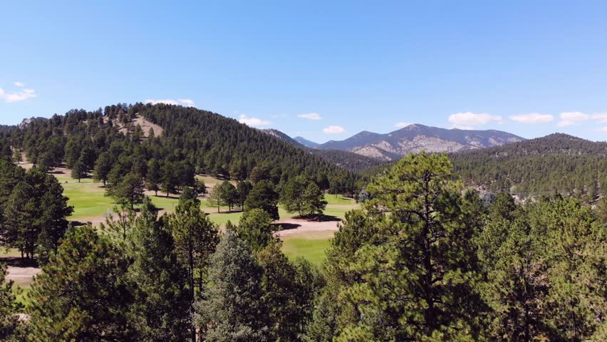 View of golf carts on golf course and kayaks on lake in the mountains on sunny day.