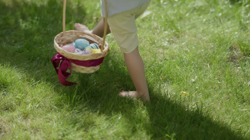 child's barefoot legs stepping green grass colorful Easter eggs in basket. traditional spring holiday celebration: little kid boy holding basket full of Easter eggs walking barefoot green lawn Royalty-Free Stock Footage #1101338041