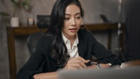 Professional Asian business woman in black suit working by talking with a partner team by using video call on laptop camera, online conference meeting by internet computer communication technology