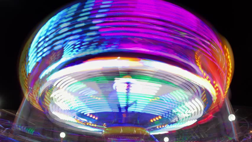 Multi Colored Illuminated Merry Go Round Carousel in Time Lapse. Bright Colorful Lights at Night in Amusement Park. Festive Having Fun and Playful at City Fair. Glowing Rotation Move on Recreation 4k Royalty-Free Stock Footage #1101341227