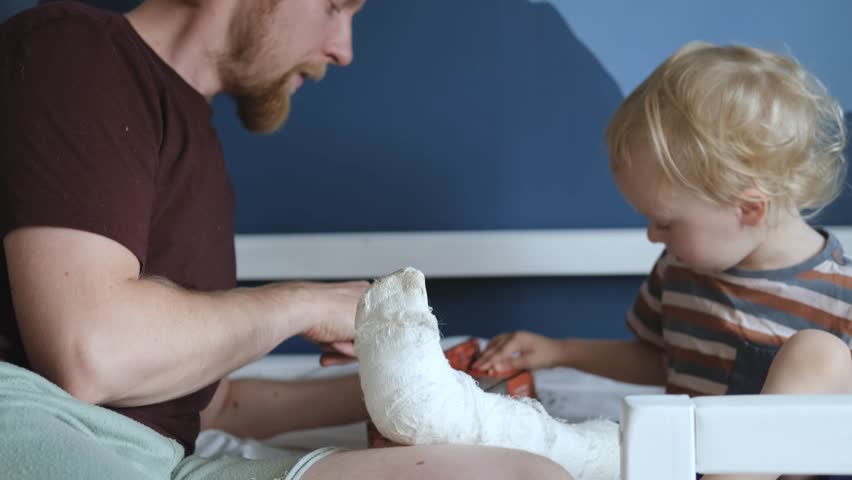 father and son with a splint on their leg play sitting on the bed