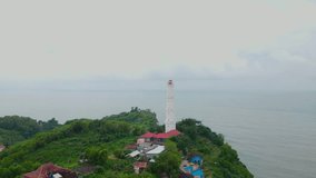 Aerial view of coral cliff overgrown by trees with white lighthouse build on it - Baron Beach, Indonesia