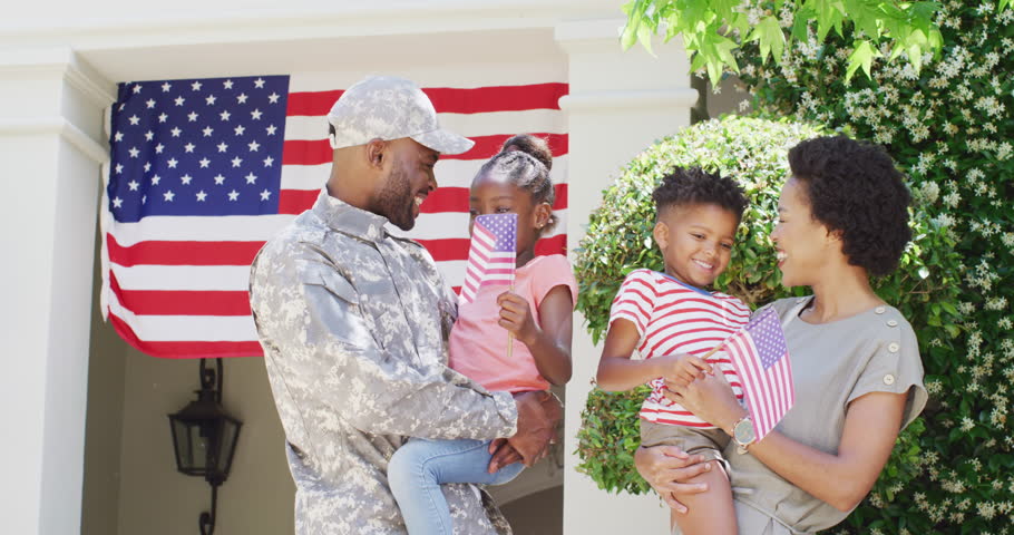 Happy african american male soldier and wife holding daughter and son outside home, slow motion. Family, military service and homecoming concept.