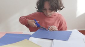 The child cuts colored paper with scissors at the table. the boy cuts a snowflake out of blue paper with scissors. children's creativity.