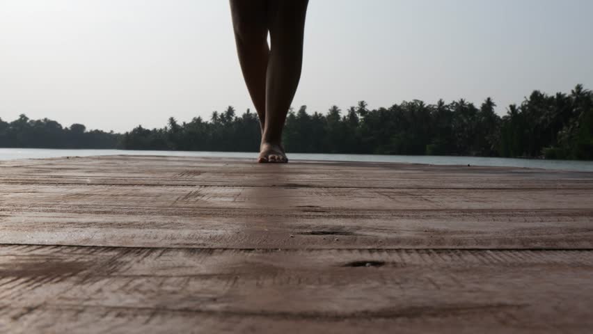 Female legs walking on wooden pier in a hot summer day.