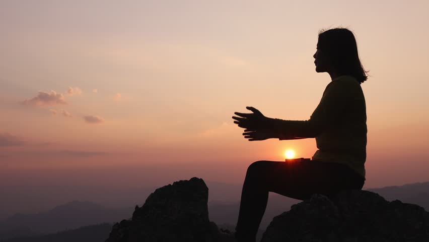 Silhouette of a woman with her palm open to worship. Sitting on a rock, the sun is rising. meditation for victory .Success on the top of the mountain Supreme faith in God. Royalty-Free Stock Footage #1101353495