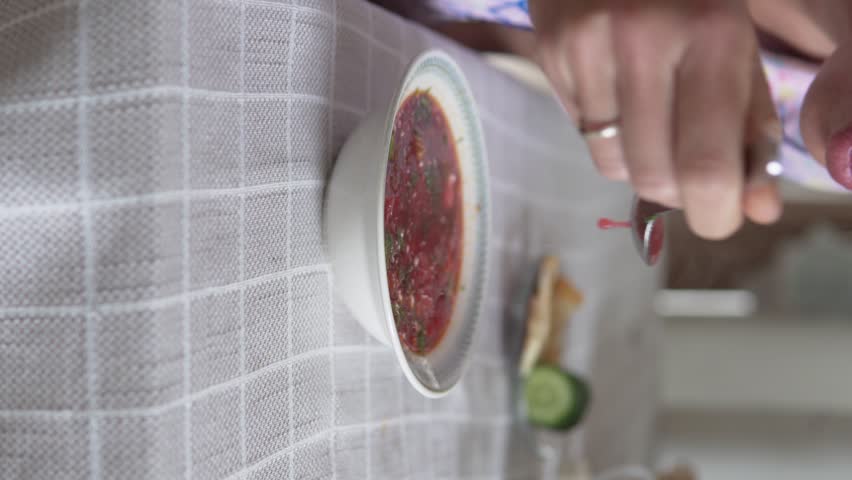 Vertical video, a man eats Ukrainian borscht at home in the kitchen.