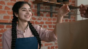 Friendly young indian woman waitress barista giving takeaway food bag to customer female seller cafe employee in apron holding takeout order delivery in cafeteria restaurant coffee shop serves client - Powered by Shutterstock - Get 15% off with code: PIKWIZARD15