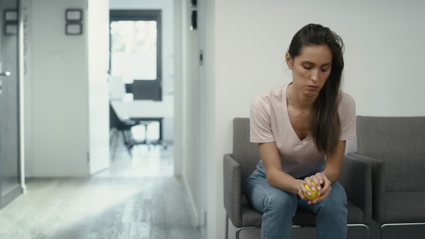 Wide shot of stressed caucasian woman sitting in clinic waiting room and squeezing a stress ball. Shot with RED helium camera in 8K. Royalty-Free Stock Footage #1101361509