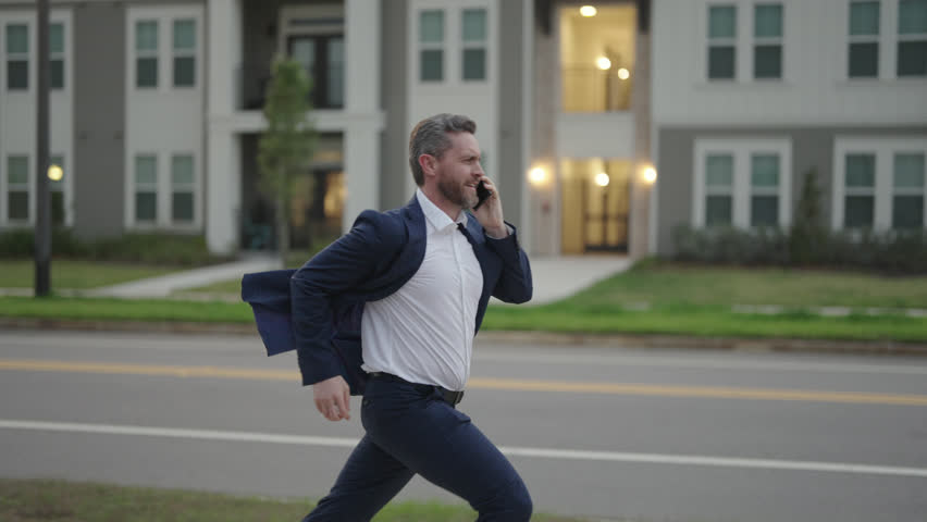 Man in suit in a hurry, calling phone and running. Running business man with phone outdoor. Running businessman talking on phone. Middle aged business man hurry late and talking on phone. Slow motion. Royalty-Free Stock Footage #1101364541