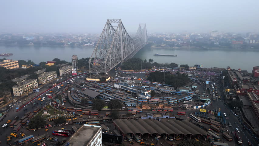 Aerial timelapse view of traffic around architectural landmark Howrah Bridge over the Hooghly River on a smoggy day in Kolkata, India, one of the world's most polluted cities. Royalty-Free Stock Footage #1101364587