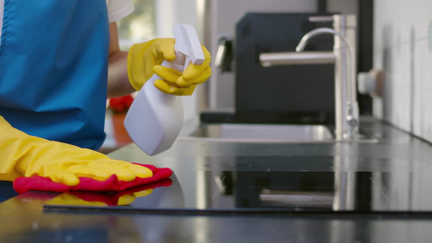 Cropped shot of maid clean kitchen surface with detergent sprayer. Housewife wash electric stove in kitchen. Janitor or professional cleaner disinfect furniture. Realtime. 