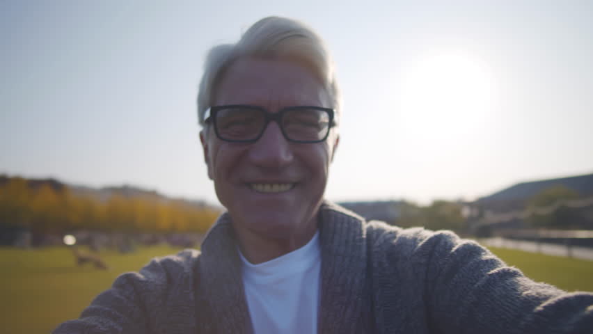 Pov shot of happy senior man spinning around outdoors. Cheerful aged man spin looking at camera. Smiling mature man move in circle in park. Realtime. 