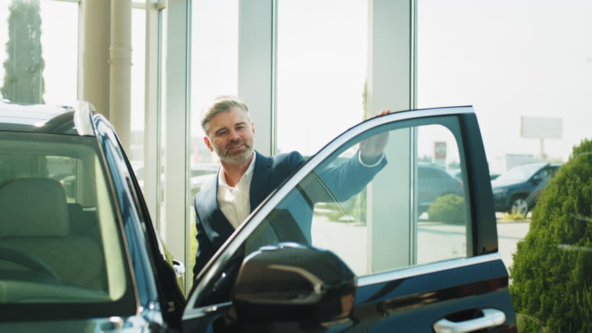 Serious thoughtful middle aged caucasian man choosing new car in dealership. Happy beard grey hair man finally gets long-awaited car, wearing formal suit. Dealership store . Sales concept. Royalty-Free Stock Footage #1101367491