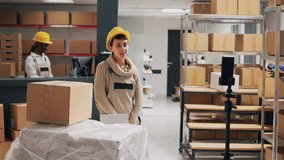 Young adult filming advertisement video in stockroom, showing products boxes on online social media page. Storage room workers using mobile phone to record PR ad, industrial goods. - Powered by Shutterstock - Get 15% off with code: PIKWIZARD15