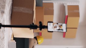Vertical video: African american girl in overalls filming PR video for social media, creating advertisement for warehouse storage in boxes. Woman recording video on smartphone, stock merchandise
