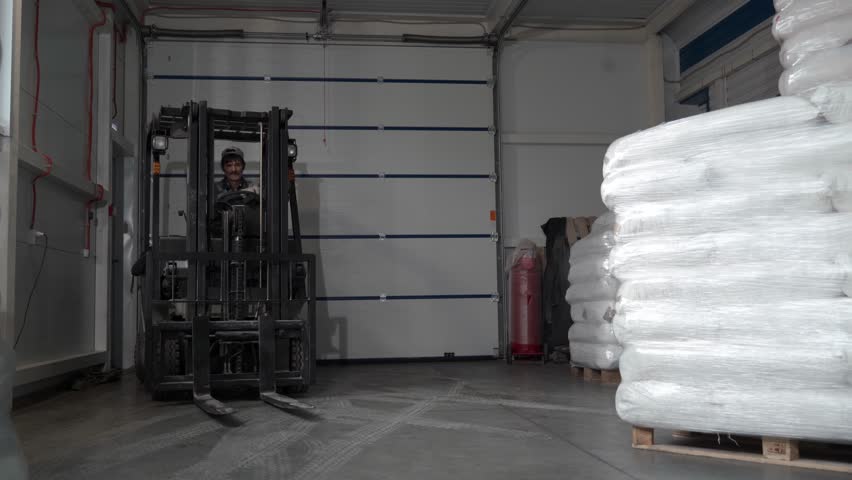 A worker in a warehouse unloads pallets with an electric forklift with sacks of flour. Adult Man works indoors on a forklift. Royalty-Free Stock Footage #1101370987