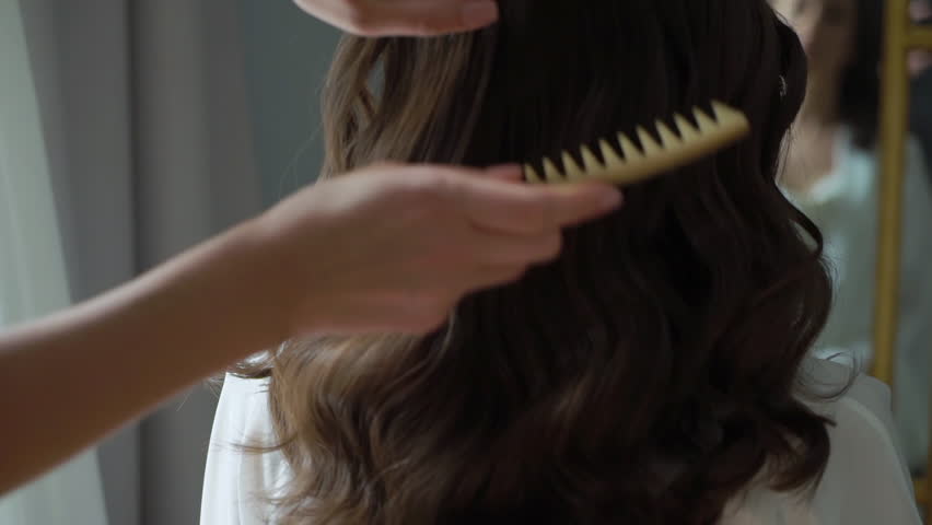 The hairdresser makes a hairstyle. Young brunette woman with dark hair. The girl combs her hair with a comb. Morning of the bride, preparing a model for a photo shoot. Royalty-Free Stock Footage #1101371081
