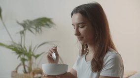 Close-up video of a woman eating porridge from a white bowl. A brunette woman in a white T-shirt has oatmeal for breakfast.