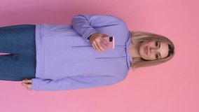 Cheerful woman with smartphone pointing aside. Vertical video.