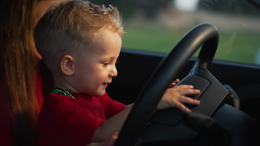 Child holds steering wheel in his hands. Child travels with his mother in car.Family travels by car. Mom teaches son to drive car.Funny kid driving vehicle.Concept of family happiness.Family education Royalty-Free Stock Footage #1101375827