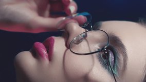 Vertical video. 90s fashion. Eyewear model. 2000s beauty look. Teen girl face with artistic makeup wearing round frame glasses in purple blue color neon light on dark. - Powered by Shutterstock - Get 15% off with code: PIKWIZARD15