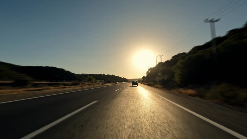 Shot behind car driving passenger sedan on road with new black asphalt at sunset or dawn. Chasing small city car on track or highway.