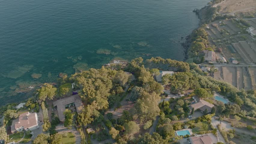 Carqueiranne; Tilting down aerial over beautiful french coastline; small waves crashing in on rocky beach; calm sea; underwater cliffs; turquoise blue water; sunny summer day; houses on coastal cliff