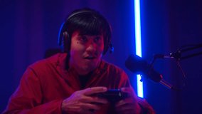 Close up Gamer man playing game and podcast steaming wearing headset with sad feeling at lose moment. Professional Streamer playing game with joystick online in dark room neon light.