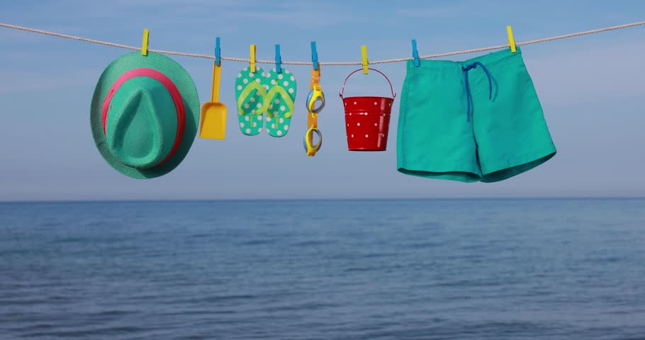 Beach objects hanging on a clothesline. Items for vacation against blue sky and sea. Summer holiday and travel concept. Slow motion | Shutterstock HD Video #1101391941