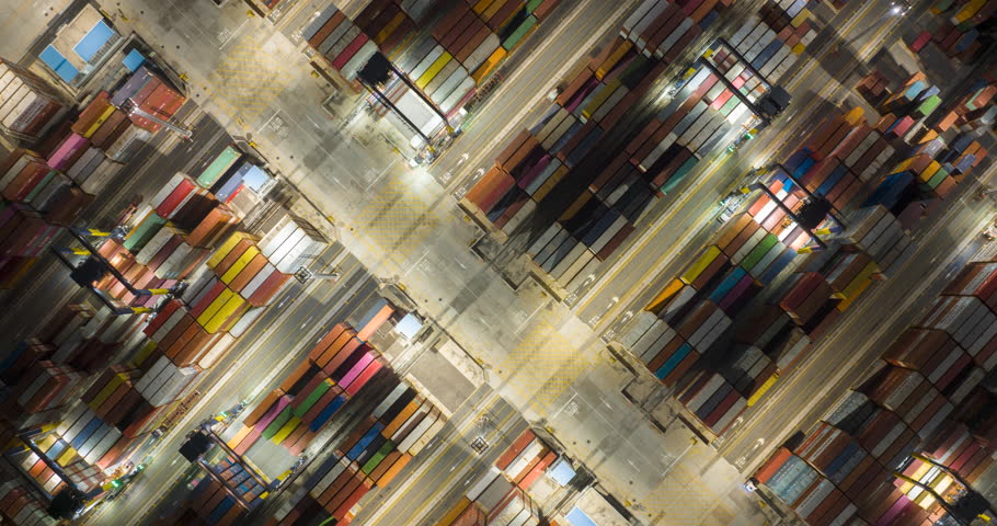 Aerial drone time-lapse top view over container terminal port loading and unloading to ship at night. Industrial shipyard being loaded containers onto a freight. import export global supply chain.