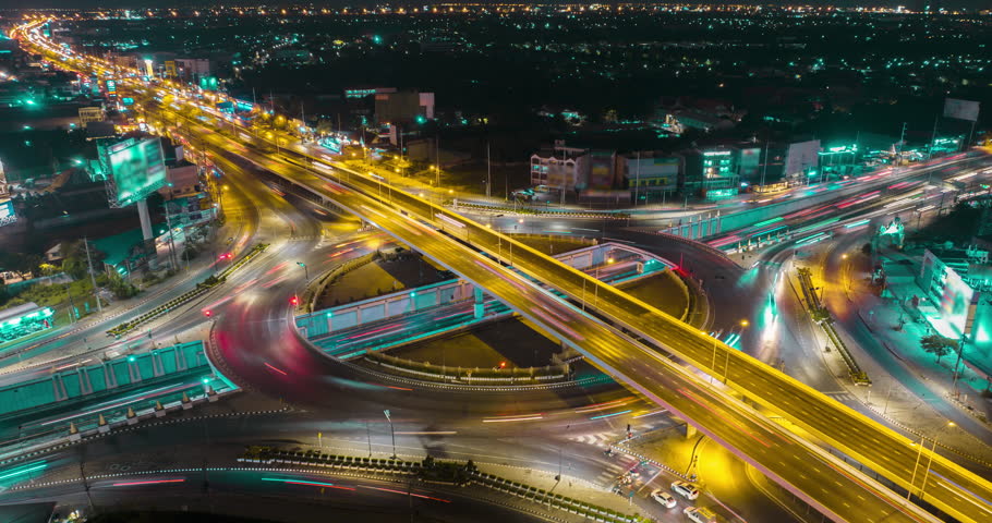 Aerial drone time-lapse of urban traffic on street intersection freeway road in capital city. Circle roundabout transportation cityscape with streaking light trail at night. High angle view timelapse. Royalty-Free Stock Footage #1101392589