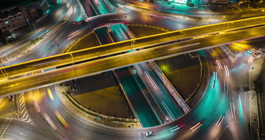 Aerial drone time-lapse of urban traffic on street intersection freeway road in capital city. Circle roundabout transportation cityscape with streaking light trail at night. High angle view timelapse. Royalty-Free Stock Footage #1101392595