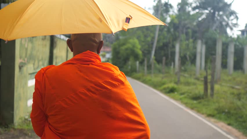 Buddhist monk walking with umbrella.