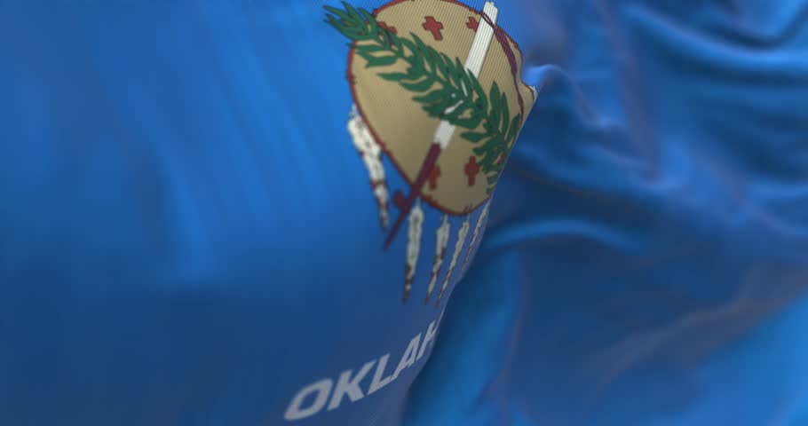 Detail of the Oklahoma state flag waving. Blue field with a buffalo-skin shield, olive branch and peace pipe. Seamless 3d render animation. Selective focus. Slow motion loop. Close-up.