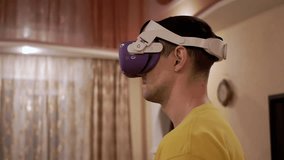 Male in 3D Glasses with Game Controllers Playing in Video Game a Room. A guy in a white helmet moving hands with a headset VR tester in room. Virtual Reality. Device. Artificial intelligence. - Powered by Shutterstock - Get 15% off with code: PIKWIZARD15