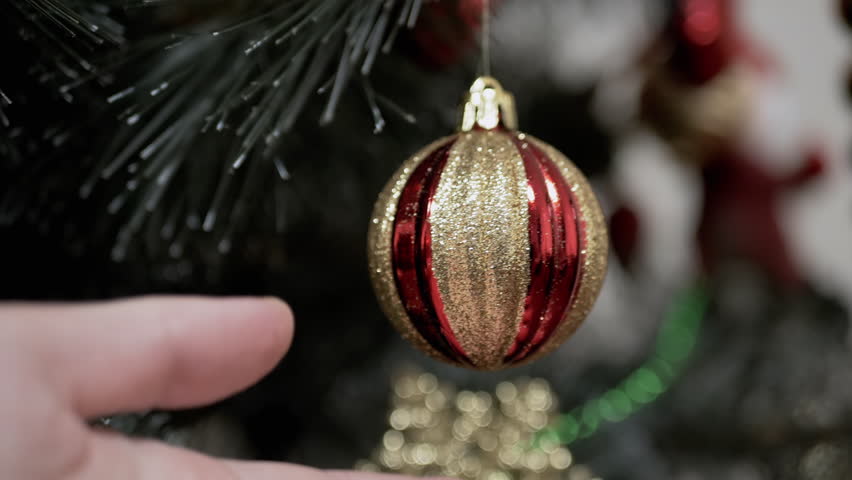 Close up, Hands Touching Christmas Tree Ball on Branch Christmas Tree. Shiny gold bauble. Christmas ornament, decoration, home decor. Holiday. Positive emotion. Concept happy family. Slow motion.