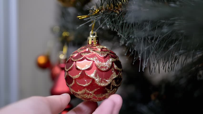 Close up, Hands Touching Christmas Tree Ball on Branch Christmas Tree. Shiny red, gold bauble. Christmas ornament, decoration, home decor. Holiday. Positive emotion. Concept happy family. Slow motion.