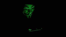 Hacker in Mask Holding a Smart Phone in Hands with a Green Screen in a Dark Room. Chroma Key. A man in an anonymous mask plays video games at night on a smartphone. Green neon light from the screen.