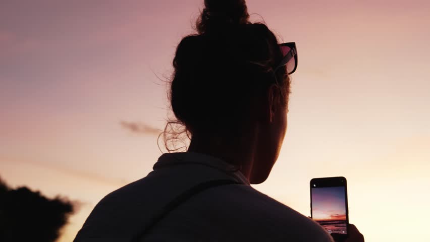 Woman Sitting Outdoors at Sea Beach Holding Mobile Phone to Make Picture. Hipster Girl at Summertime Break on Coastline Side Taking Footage for Social Media. Female in Ocean Wind of Seashore Nature 4k Royalty-Free Stock Footage #1101402781
