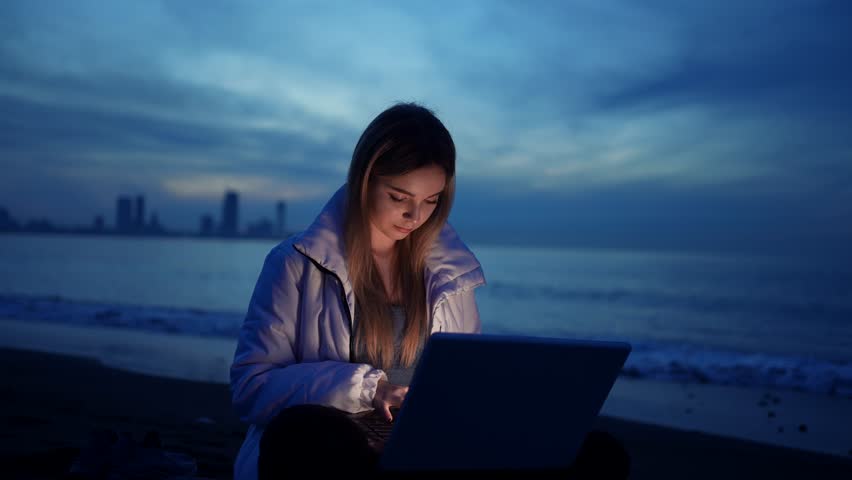 portrait female freelancer is using a laptop on the beach of the sea in the evening