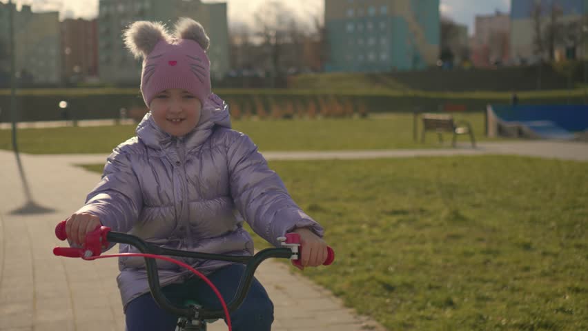 Cute child enjoy bike ride in city park during her spring vacation. Smiling cyclist girl makes most of her leisure time slow motion. Happy childhood, sports outdoors in playground