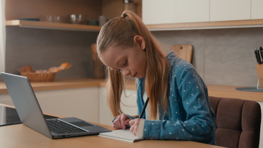 Cute primary Caucasian school girl studying at kitchen with laptop. Child daughter kid schoolgirl pupil doing homework writing exercise distance learning. Children home education e-learning quarantine Royalty-Free Stock Footage #1101405321