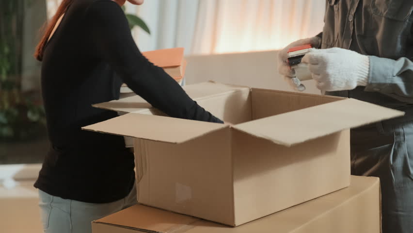 Cropped shot of woman packing books into carton box and moving service worker sealing it with adhesive tape while preparing for leaving house | Shutterstock HD Video #1101410065