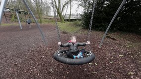 Slow Motion Video of a Young boy having fun in a playground swinging and laughing surrounded by autumn leaves. UK