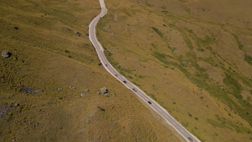 Cars driving up Cardrona Mountain Pass in Otago, New Zealand - aerial tilt up