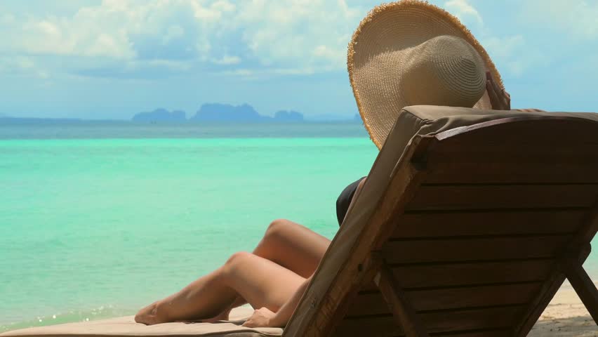Unrecognizable young woman in a bikini and hat relaxing on a comfortable lounger beach chair, overlooking the turquoise waters of a tropical paradise. Summer tropical getaway. Royalty-Free Stock Footage #1101412061
